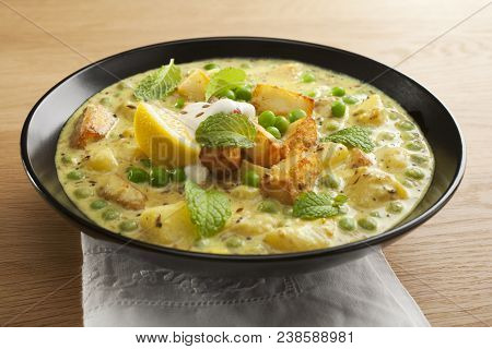Vegetarian Curry, Panir And Peas, Garnished With Mint, Lemon And Yoghurt, In A Black Bowl On A Woode