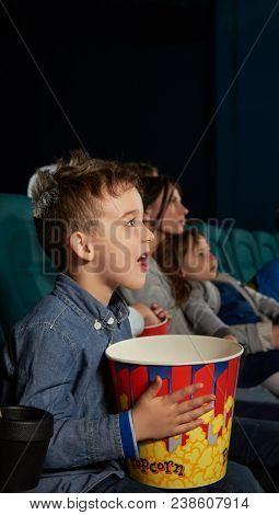 Cute Boy With Open Mouth And Steadfast Eyes Watching Film In Modern Movie Theatre. Small Viewer Hold