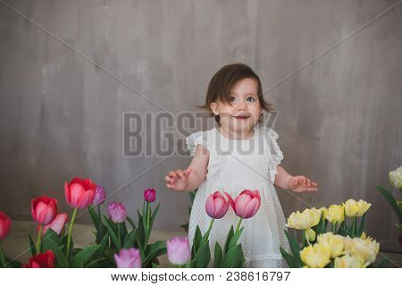 Beautiful Smiling Little Girl In White Lace Dress Among Tulips.