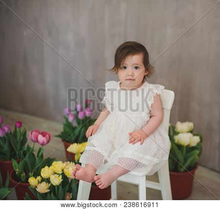 Beautiful Smiling Little Girl In White Lace Dress Among Tulips.