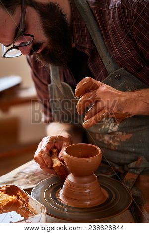 Close-up Hands Of A Male Potter In Plaid Shirt And Dirty Apron Who Molds A Vase From Clay, Selective