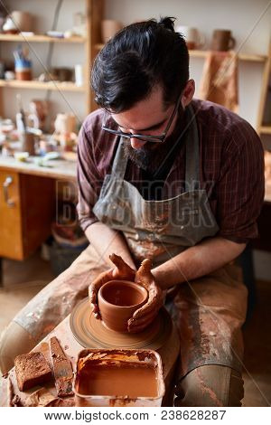 Portrait Of A Handsome Bearded Male Potter In Plaid Shirt And Dirty Apron Who Molds Bowl From Clay, 