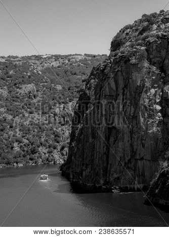 A Cruise Boat Navigates Just Near The Foot Of A Huge Cliff.