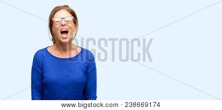 Middle age woman wearing wool sweater and glasses stressful, terrified in panic, shouting exasperated and frustrated. Unpleasant gesture. Annoying work drives me crazy isolated blue background
