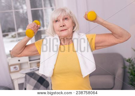 Strenuous Exercise. Pleasant Senior Woman Lifting Up Dumbbells And Looking Tired Of The Exercise Whi