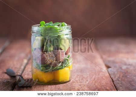 Hawaiian Poke Salad With Tuna, Avocado And Vegetables In A Jar With A Fork On A Brown Rustic Backgro
