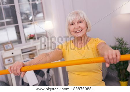 Great Mood. Cheerful Elderly Woman In A Yellow T-shirt Holding A Health Bar In Front Of Her And Smil