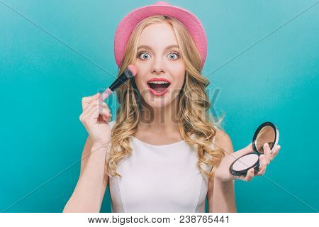 Happy Girl With Blonde Hair Wears Pink Heat. She Has Some Cosmatics In Her Hands. Girl Is Putting So