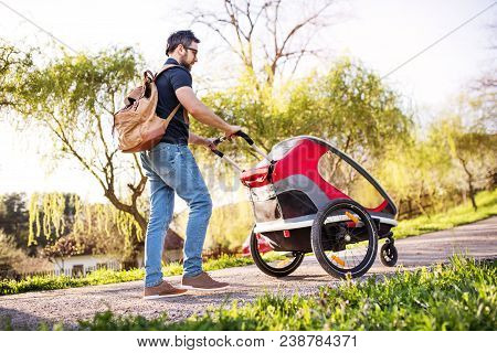A Father With Backpack And Jogging Stroller On A Walk Outside In Spring Nature.