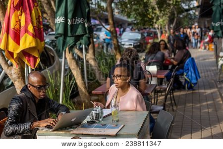 Johannesburg, South Africa, April 29-2018: Couple Sitting At Street Cafe Working On Laptop.