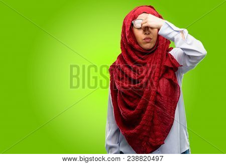 Young arab woman wearing hijab with sleepy expression, being overworked and tired, rubbes nose because of weariness