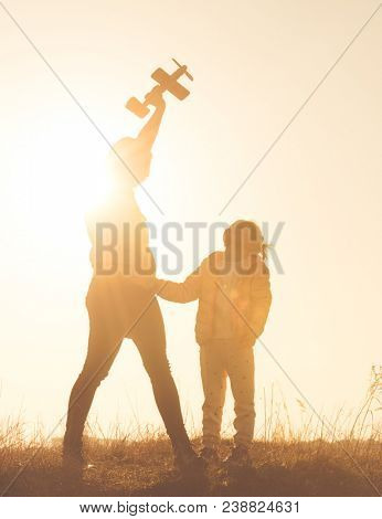 Silhouette of mother and daughter playing in the field with small airplane toy against vivid orange sky. Happy mother and daughter at sunset time