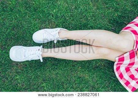 Woman Legs In White Shoes Green Grass On Background