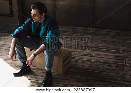 Handsome Young Man In Vintage Windcheater Sitting On Wooden Box In Loft Room