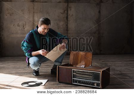 Happy Nostalgic Young Man In Vintage Windcheater With Vinyl Record Player