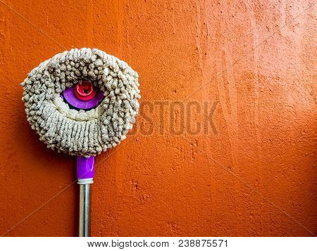 Round Broom Cloth Mop Rotary Violet Handle Leaned On Orange Wall As Background With Space For Text