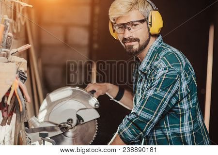Young Hipster Bearded Man By Profession Carpenter Builder Saws With A Circular Saw A Wooden Board On
