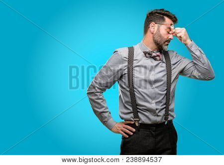 Middle age man, with beard and bow tie with sleepy expression, being overworked and tired, rubbes nose because of weariness