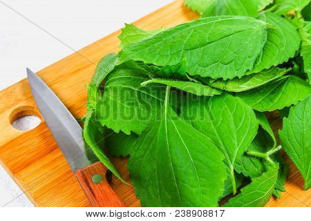 Leaves Of Fresh Green Nettle On A Cutting Wooden Board With A Knife On A Gray Concrete Table