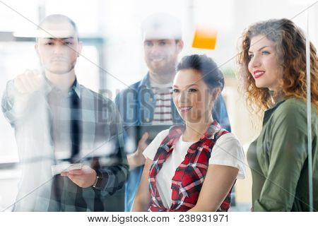 business, startup, planning and people concept - happy creative team writing on glass board at office