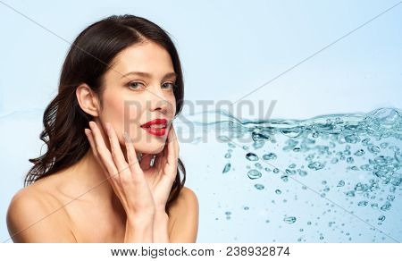 beauty, make up and skin moisturizing concept - happy smiling young woman with red lipstick touching her face over blue background and bubbles in water 