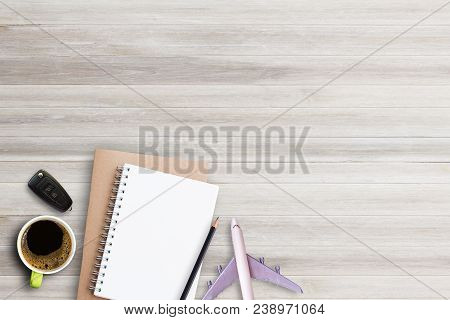 Notebook,pencil With Cup Of Coffee,car Key And Airplane On White Wooden Table Background. Top View W