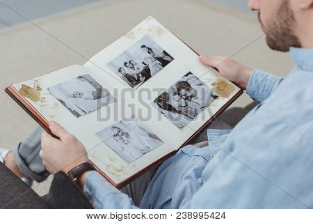 Partial View Of Man With Photo Album In Hands Resting On Sofa At Home