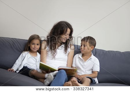 Family Ideas And Concepts. Mother Reading A Book Together With Her Little Children On Couch Indoors.
