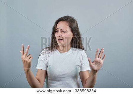 Girl In White T-shirt Looks At Her Three Fingers, With Another Hand Shows Woman Five. Behind Her The