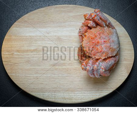 Icy Hairy Crab Laying On The Black Table And Oval Wooden Cutting Board, Top View With Copy Space.