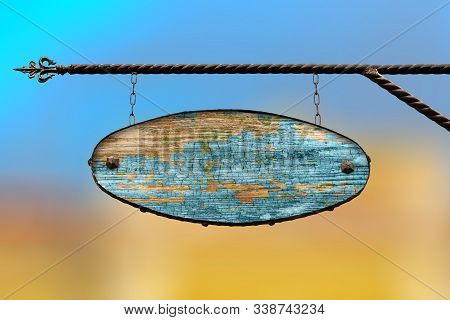 Oval Wooden Blue Sign. An Old Tattered Wooden Shopboard With No Text Hanging On A Wrought Iron Struc