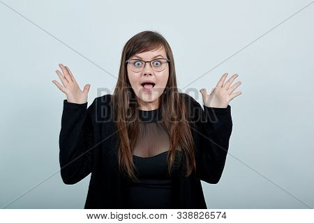 Surprised Cheerful Young Woman In Casual Black Dress, Opened Mouth, Spreading Hands Isolated On Gray
