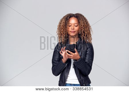 Studio Shot Of Woman Wearing Leather Jacket Using Mobile Phone