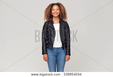 Three Quarter Length Studio Shot Of Happy Young Woman Wearing Leather Jacket Smiling At Camera