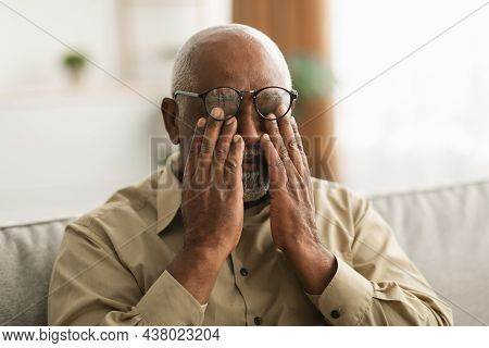Senior African Man Rubbing Eyes Wearing Eyeglasses Having Glaucoma Indoors