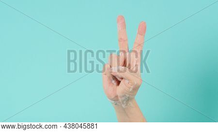 Hand Is Do Peace Or Good Luck Sign And Have Foam Soap Bubbles On A Green Mint Background