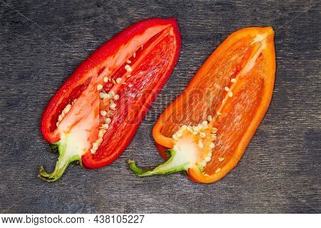 Two Halves Of The Fresh Bell Peppers Red And Orange Colors Cut Lengthwise Lie On The Dark Surface, T