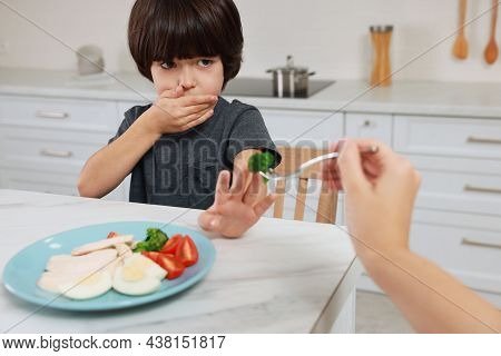 Mother Feeding Her Son In Kitchen, Closeup. Little Boy Refusing To Eat Dinner
