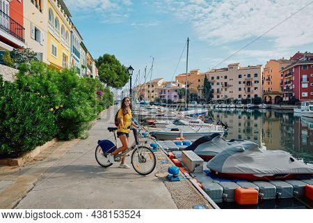 Smiling Woman Tourist With Bicycle On Pier With Yachts And Boats At Beautiful Harbor Of Port Saplaya