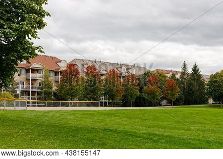 Residential House With Apartments Or Condo Building Near Park With Baseball Field In Autumn Season.