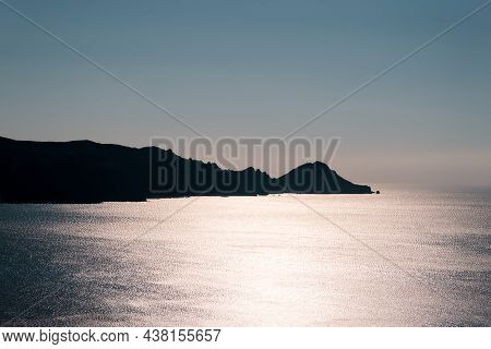 Capu Rossu Headland On The West Coast Of Corsica Silhoutted Against The Mediterranean Sea Shimmering
