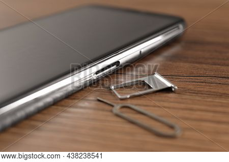 Sim Card Tray, Mobile Phone And Ejector Tool On Wooden Table, Closeup