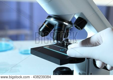 Scientist Examining Sample Of Light Blue Liquid On Slide Under Microscope In Laboratory, Closeup
