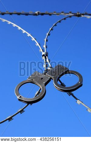 Old Metal Handcuffs Hanging On Razor Wire Against Blue Sky