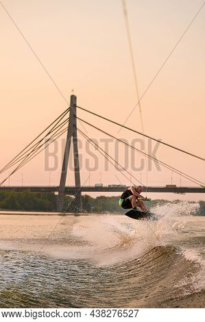 Energy Man Holds Rope And Jumps On Wakeboard On City Bridge Background.