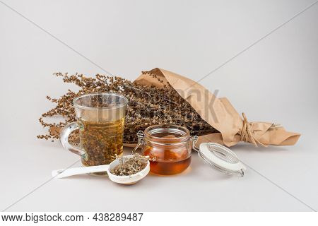 Glass Of Herb Tea, Tea Strainer, Honey And Wormwood Twigs Wrapped In Brown Paper.