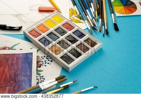 A Box Of Watercolors With Brushes. Draw, Background. Packing Of Multicolored New Paints On The Table