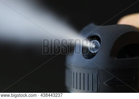 Close-up Of Spraying Perfume In Motion On Black Background. Macro Shot Of Finger Pressing Bottle But