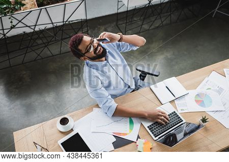 Top View Of Positive African American Businessman Talking On Smartphone Near Gadgets, Coffee And Doc