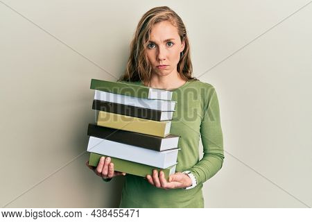 Young blonde woman holding a pile of books skeptic and nervous, frowning upset because of problem. negative person. 